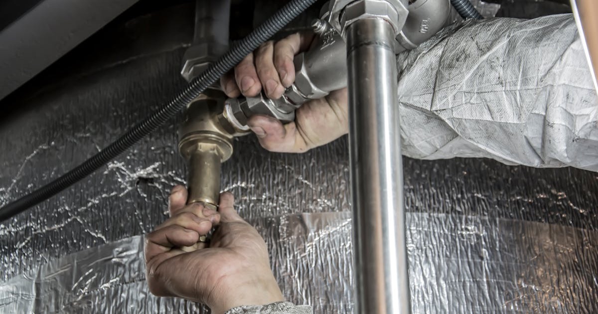 Close-up of a plumber's hands installing steel pipes indoors, showcasing skilled manual work.