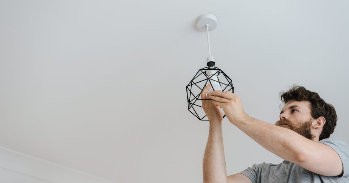 A professional electrician skillfully installing a modern geometric ceiling lamp indoors.