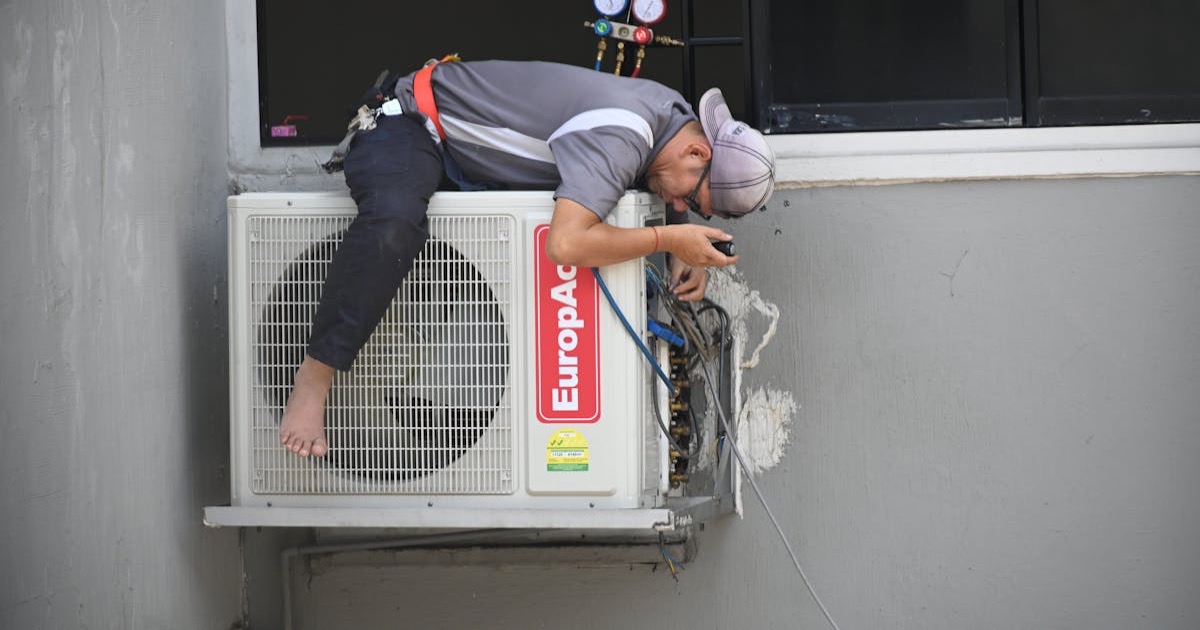 A technician skillfully repairing an outdoor air conditioning unit mounted on a building wall.