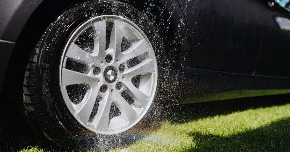 Dynamic image of a car wheel being hosed down during a wash on green grass.