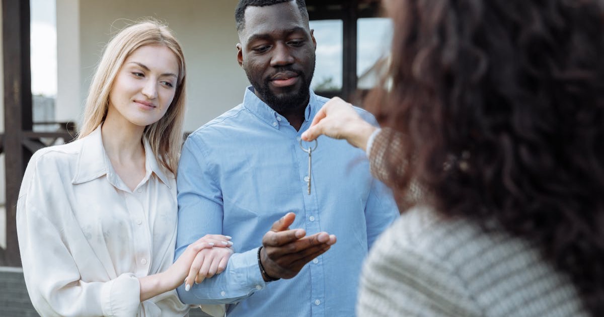 Happy couple receiving keys to their new home from real estate agent outdoors.
