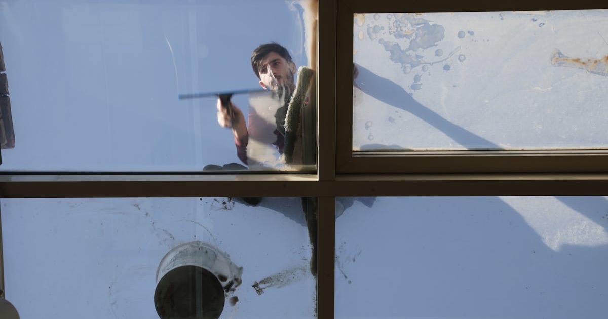 A male window cleaner washing the exterior glass roof from above with a tool during daylight.