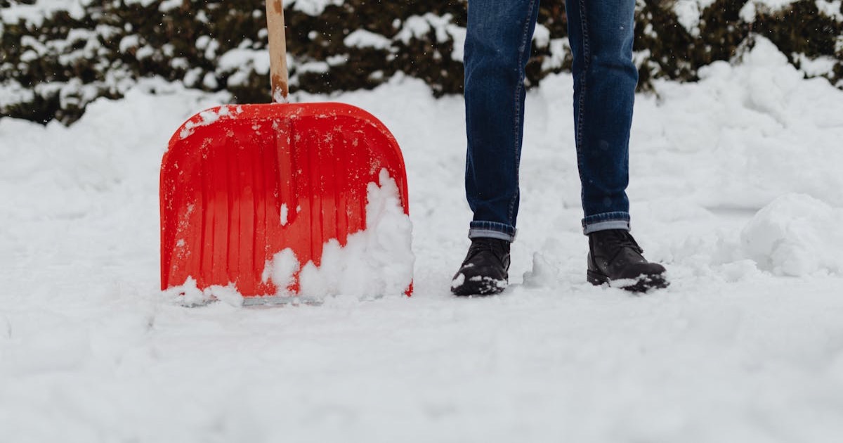 A person shoveling heavy winter snowfall using a red snow shovel. Outdoor winter scene.