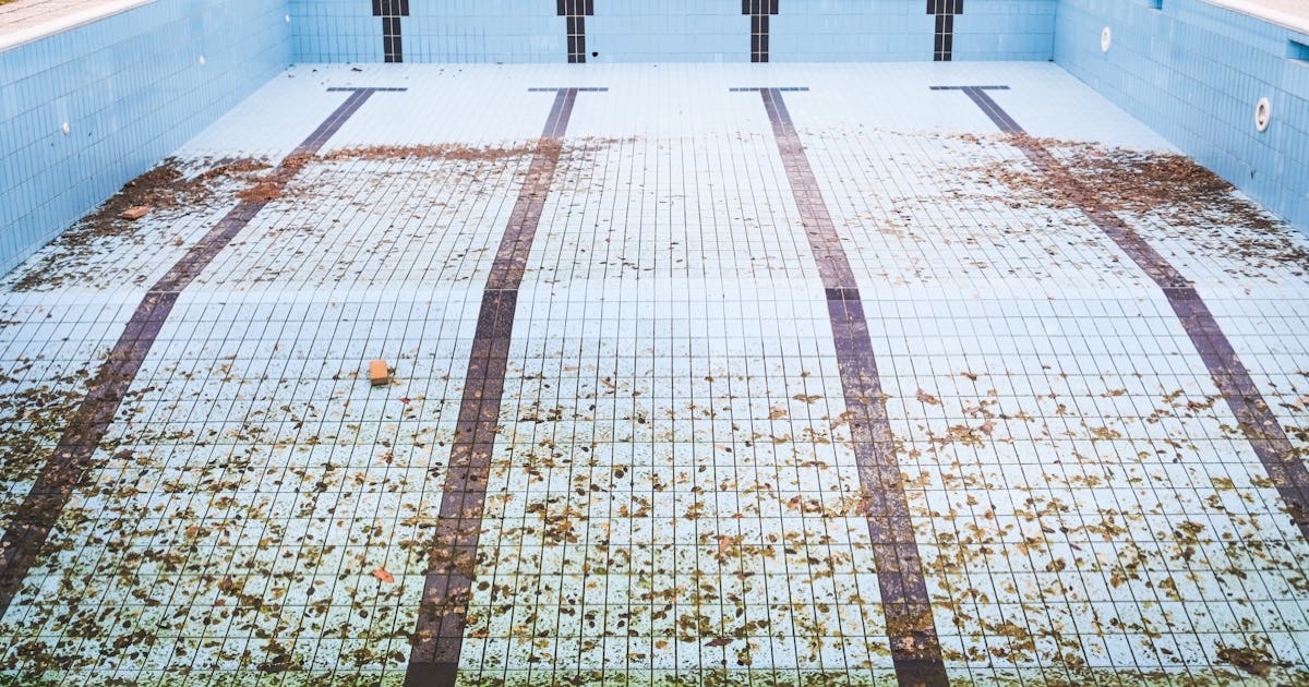 High angle view of an empty, abandoned swimming pool with leaves scattered on the tiled surface.